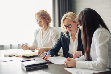Three caucasian female students or interns in white shirts , intern using laptop, working on pc,...