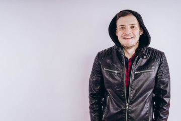 Man in trendy jacket on white background. Portrait of young male in leather jacket zipping up and smiling at camera on white background