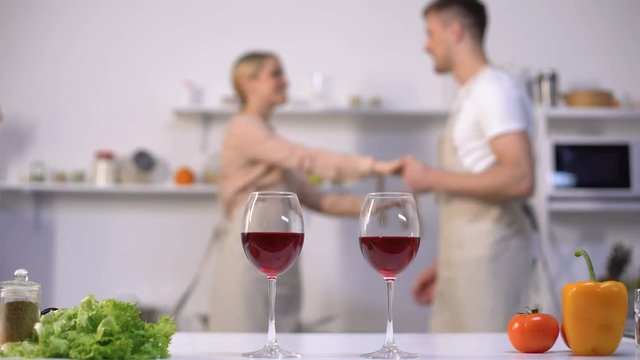 Wine glasses on table, family couple dancing on background, kitchen interior