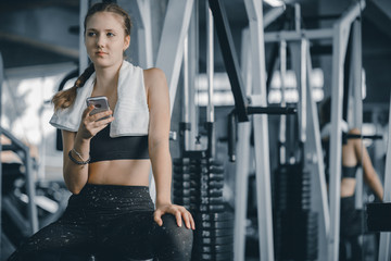 Fototapeta premium Szczęśliwy młodych atrakcyjnych kobiet fitness za pomocą smartfona odpoczywa w siłowni podczas porannych ćwiczeń. Relaks po ciężkim treningu na siłowni. Zdrowy styl życia sportowego, koncepcja fitness.