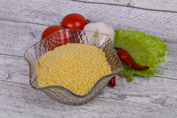 Raw couscous in the bowl served salad leaves, tomato and pepper