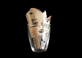 Torn musical notes in a glass, pieces of paper, isolated on black background