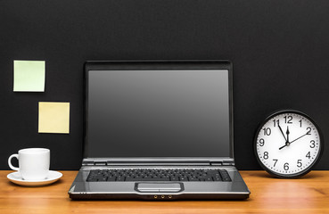 Laptop with blank screen, cup of coffee and clock at office workplace. Front view. Space for text.