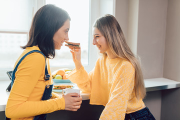 happy friends eating hamburgers, drinking tea, blond girl treating her friend with a snack. close up photo