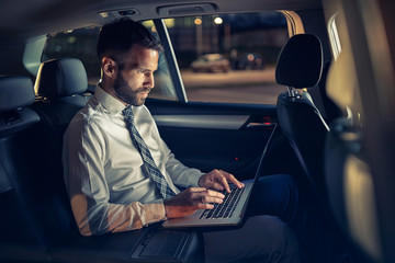 serious businessman working late in car on laptop.