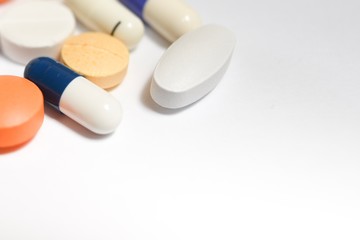 A close-up photo of various medical pills and capsules spilt on white background