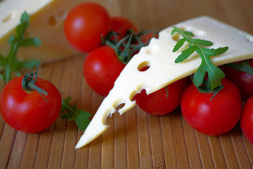 Slice of cheese with tomatoes and herbs on wooden mat.