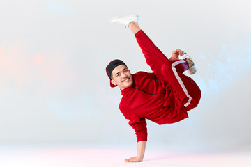 Stylish dressed in red sweatpants asian b-boy is performing kick in air, standing on hands while dancing break dance on white background. Freestyler doing air baby freeze