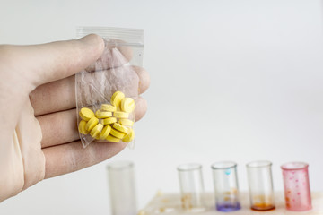 study of synthetic drugs: a scientist holds a sample of a new drug above the table with other...