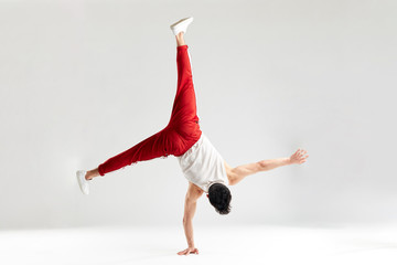 Break dancer doing handstand stunt on one hand and splitted out legs over white studio background