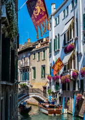 Venice street canal with gondola, old bridge and houses with venecian flags and flowers, Italy