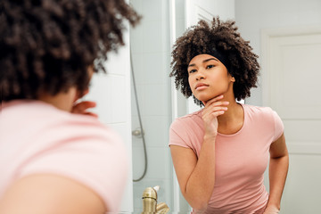 Fototapeta na wymiar Beautiful young woman inspecting her skin in the bathroom mirror at home
