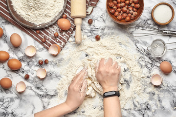 Close-up shot. Top view of a baker cook place, hands are working with a raw dough on the marble table background.