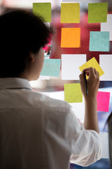 Shot of businessman holding pencil and writing on sticky note.