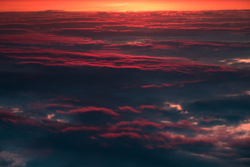 Flying above dark clouds in red sky at sunrise