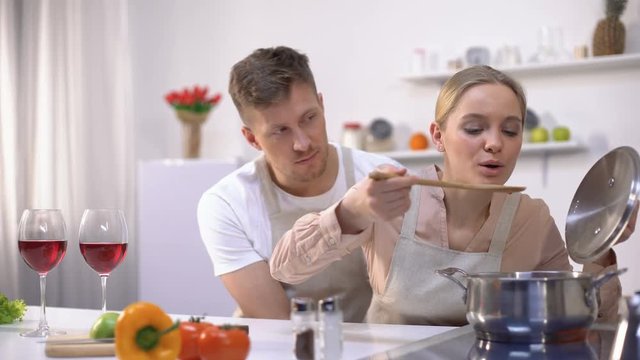 Happy couple cooking together in kitchen, female tasting soup, healthy food