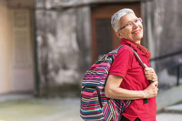 Senior old woman tourist with a backpack preparing to leave her home to go travelling