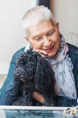 A senior old woman petting her puppy, a black mini poodle, smiling and enjoying its company