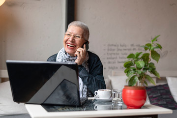 Senior old woman sitting in a coffee shop and having a nice chat over her cell phone