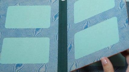 Closeup view of old vintage paper photo album with empty green spaces instead of photos. Woman turning pages. 