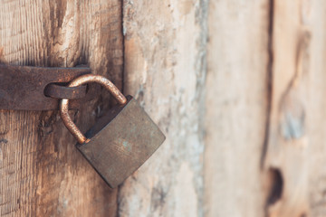 The old and vintage metal padlock with rust on the wooden door, locked for security