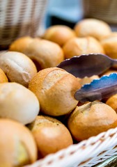 Close up of freshly baked, warm and tasty traditional bread buns in a basket with serving tongs on a luxury breakfast buffet