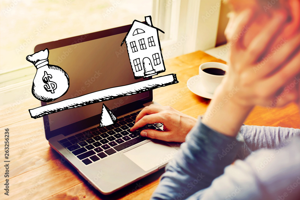 Poster house and money on the scale with man using a laptop computer