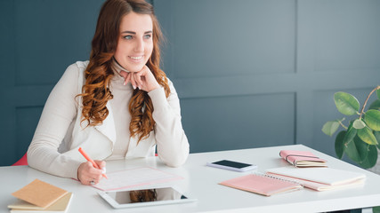 Scheduling agenda. Ambitious business plans. Smiling young woman thinking and writing. Workplace, tablet, smartphone