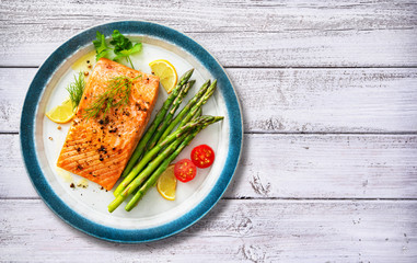 Grilled salmon steak garnished with green asparagus, lemon and tomatoes