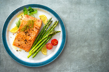 Grilled salmon steak garnished with green asparagus, lemon and tomatoes