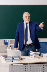 Aged male teacher in front of chalkboard 