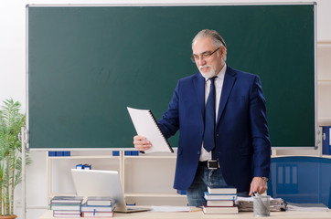 Aged male teacher in front of chalkboard 