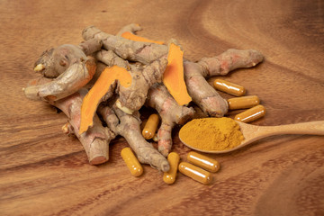 selective focus image of turmeric powder in wooden spoon,  turmeric root rhizome which some slice yellow pieces and turmeric capsule on wooden board