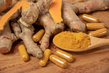 selective focus image of turmeric powder in wooden spoon,  turmeric root rhizome which some slice yellow pieces and turmeric capsule on wooden board