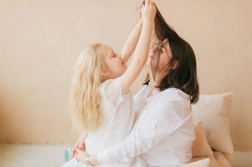 Obraz na płótnie Canvas Mother and daughter indoor lifestyle portrait. Mom with child have fun on abstract background. Happiness of motherhood. Mother hugs with her little daughter. Young emotional girl playing with mom.