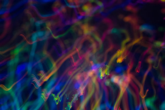 Blurred neon lights in motion. Thin curved multicolor lines on dark background. Lens flare effect.