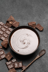 ceramic bowl of chocolate cream or melted chocolate and pieces of chocolate isolated on dark concrete background