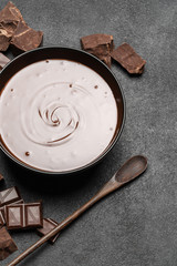Fototapeta premium ceramic bowl of chocolate cream or melted chocolate and pieces of chocolate isolated on dark concrete background