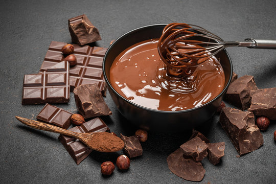 ceramic bowl of chocolate cream or melted chocolate and pieces of chocolate on dark concrete background