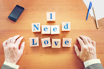 I need love. Businessman made text from wooden cubes on a desk