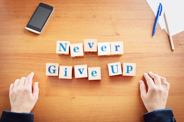 Never give up. Business woman made text from wooden cubes on a desk