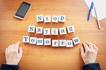 Stop saying tomorrow. Business woman made text from wooden cubes on a desk