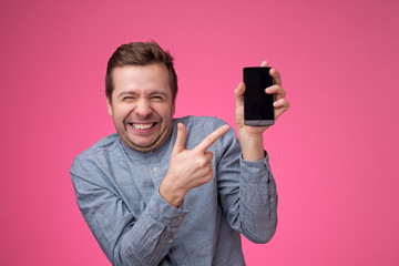 Funny young european man pointing to phone screen of his smartphone
