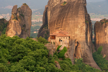 Fototapeta na wymiar Magnificent spring landscape.Orthodox Monastery of Rousanou (St. Barbara), immense monolithic pillar, green foliage at the background of stone wall in Meteora, Pindos Mountains, Thessaly, Greece.