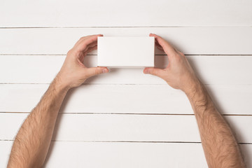 White rectangular box in male hands. Top view. White table on the background