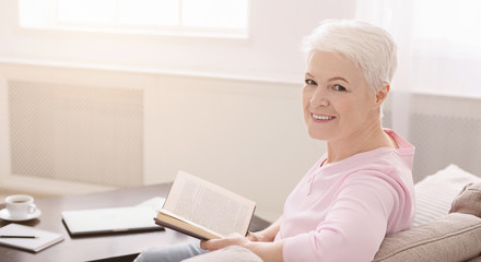 Portrait of smiling senior woman with book on sofa at home