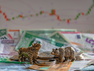 Bronze figures of a bull and a bear near metal coins against the background of paper money and...
