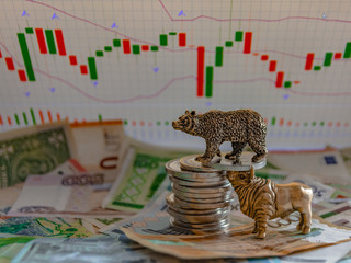 Bronze figures of a bull and a bear near metal coins against the background of paper money and...