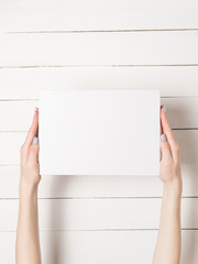 White rectangular box in female hands. Top view. White table on the background