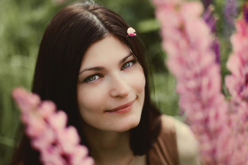 Portrait of a beautiful girl with long dark hair and green eyes in a field of lupine flowers.